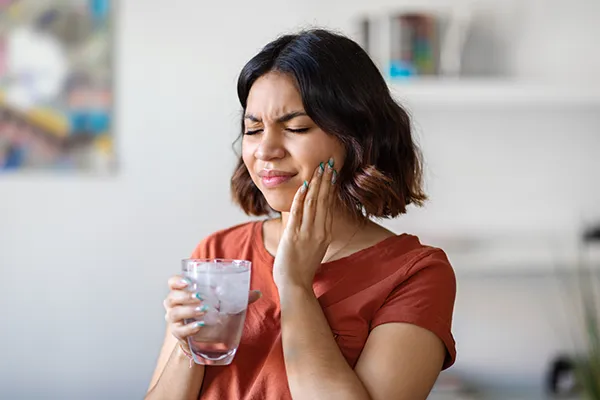 Young woman rubbing her jaw and wincing in pain before emergency treatment at Highridge Dental Care in Folsom, CA