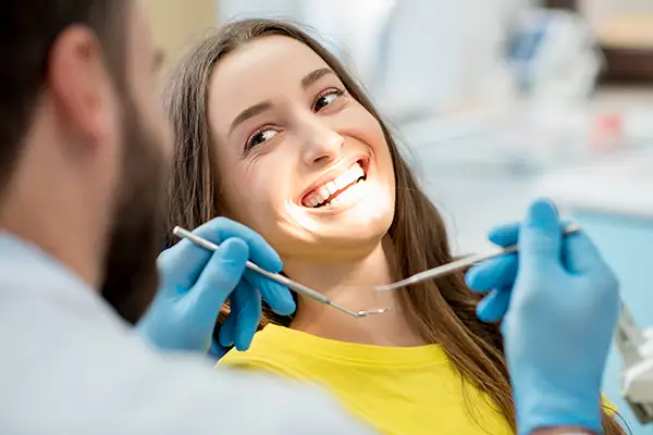 Woman smiling brightly while undergoing a dental checkup, demonstrating the importance of regular dental visits for preventive care.